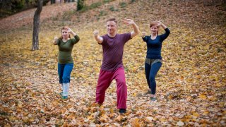 Szabadban mozog több ember, elöl egy, aki vezeti a csoportot, jóga, tai chi, chikung, pilates mozgásokat végeznek csoportosan.